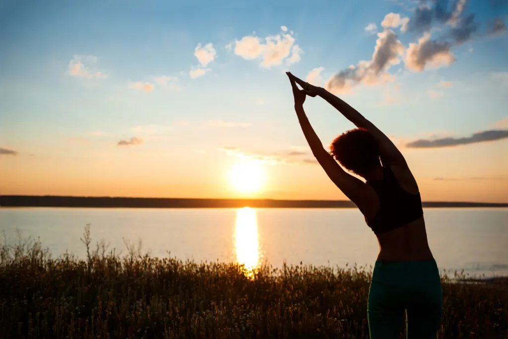 Femme bras levés face au coucher de soleil